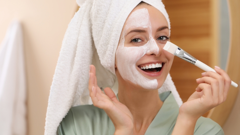 Žena nanosi masku za lice četkicom dok drži peškir omotan oko glave nakon tuširanja