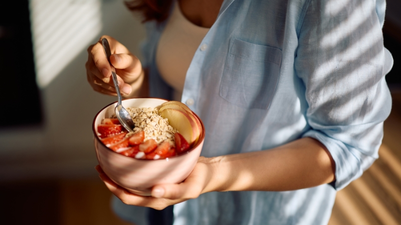 Žena drži činiju sa ovsenim pahuljicama, jagodama i jabukom kao zdrav proteinski doručak