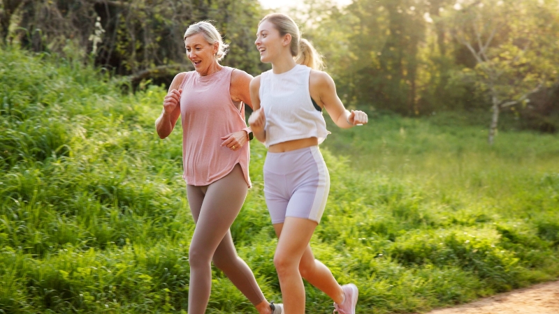 Dve žene trče kroz prirodu, nasmejane i u pokretu